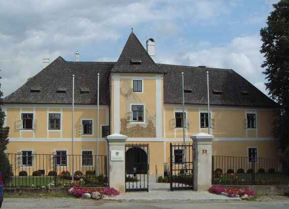 Blick auf das Gebäude des Instituts von vorne, es handelt sich um ein Schloss in Petzenkirchen. Im Vordergrund ist ein Zaun mit Tor. Das Tor ist links und rechts in zwei großen Säulen verankert. Das Gebäude besteht aus einem etwas höheren Mittelteil (drei Etagen hoch) und zwei Seitenteilen mit jeweils zwei Etagen).