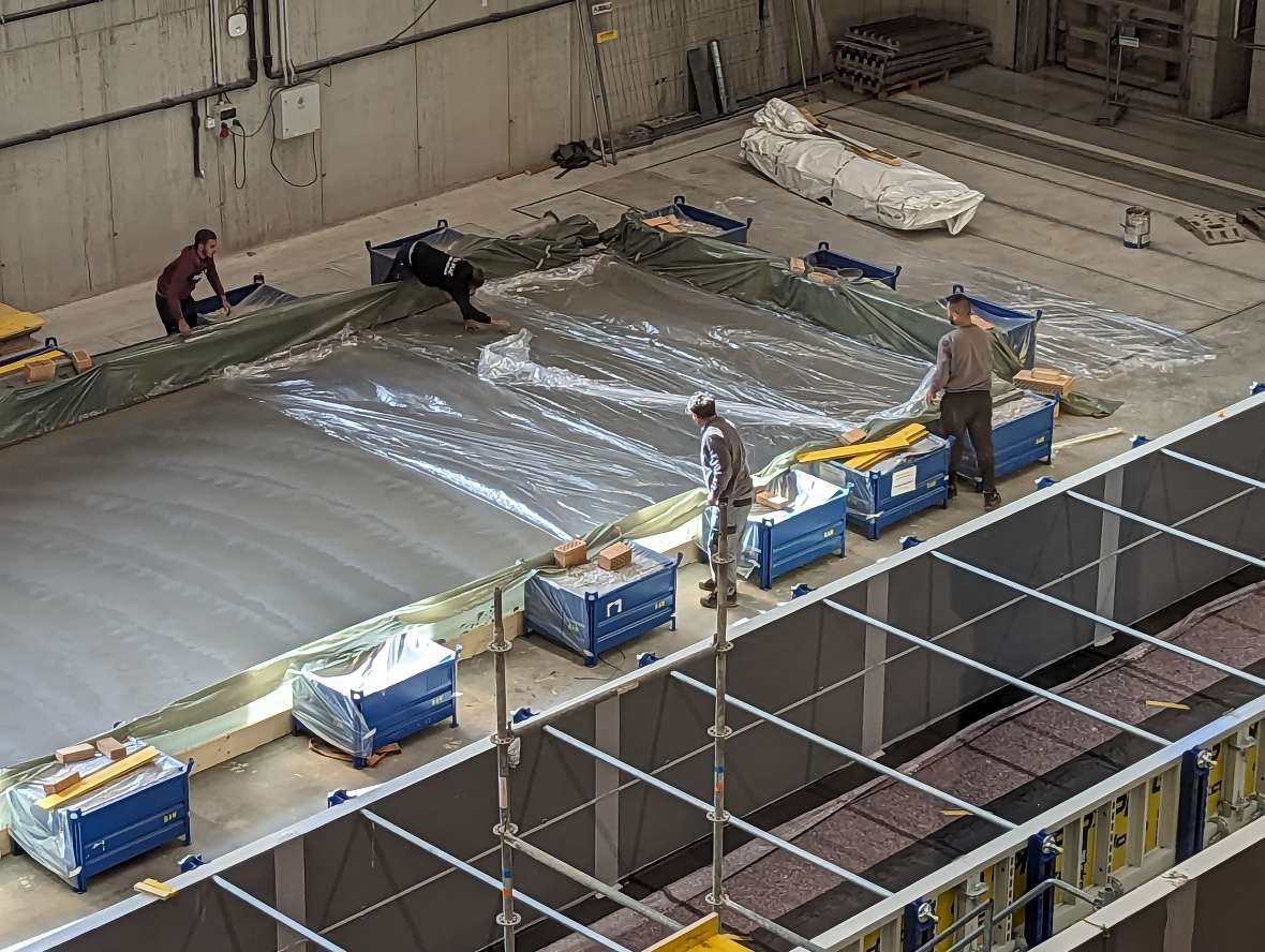 Vier Personen bedecken den fertig geglätteten Beton mit einer Kunststofffolie, damit er nicht zu schnell austrocknet.