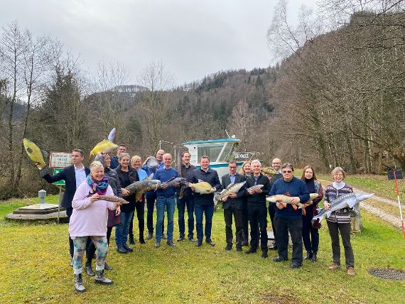 Die Teilnehmer:innen der Sektionsklausur stehen auf einer Wiese und halten Fischstofftiere in den Händen. 