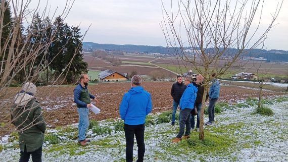 Die Teilnehmer:innen stehen auf einem Feld - Erkundung naturbasierter Lösungen wie Fruchtfolge, Feldbegrünung, Grünstreifen, Agroforst, Hecken und Rückhaltebecken.